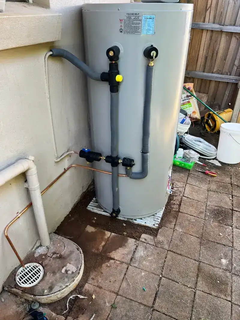 A newly installed external storage hot water unit with fresh copper pipework, isolation valves and a relief line