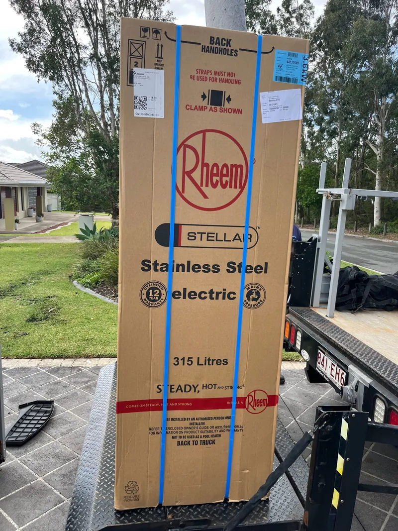 A boxed Rheem Stellar 315 litre stainless steel electric hot water system on a truck tailgate at a job site
