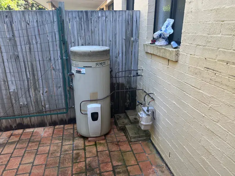 An external storage hot water unit in a brick courtyard with its relief line and pipework