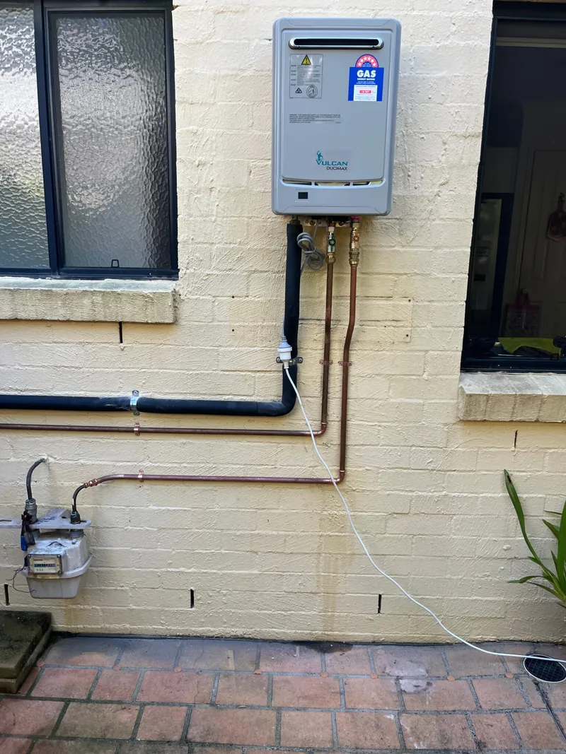 Rinnai continuous flow gas hot water unit mounted on a brick wall with new copper pipework and a gas meter below