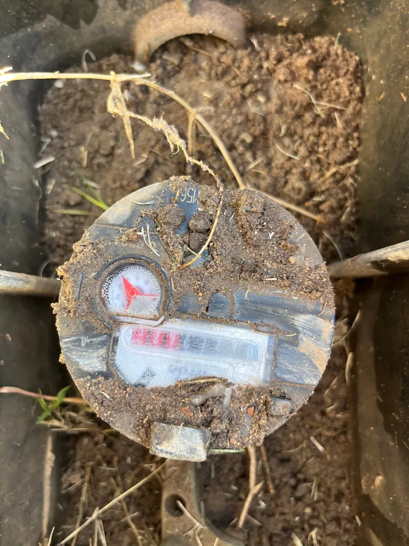 A residential water meter uncovered in the ground, being read to trace a hidden leak